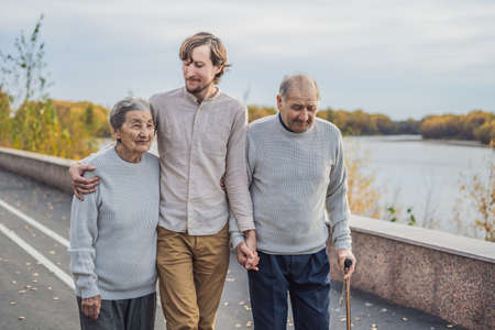 An elderly couple walks in the park with a male assistant or adult grandson. Caring for the elderly,...