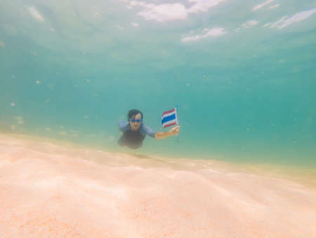 Happy man in snorkeling mask dive underwater with tropical fishes with thailand flag in coral reef sea pool.の写真素材