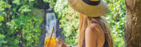Closeup portrait image of a beautiful woman drinking ice tea with feeling happy in green nature and waterfall gardenの写真素材