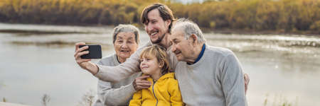 BANNER, LONG FORMAT Senior couple with with grandson and great-grandson take a selfie in the autumn park. Great-grandmother, great-grandfather and great-grandsonの写真素材