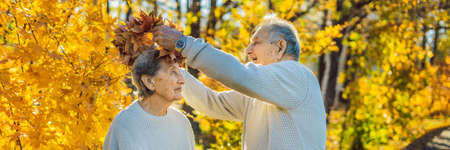 BANNER, LONG FORMAT Happy old couple having fun at autumn park. Elderly man wearing a wreath of autumn leaves to his elderly wifeの写真素材