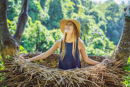 Bali trend, straw nests everywhere. Young tourist enjoying her travel around Bali island, Indonesia. Making a stop on a beautiful hill. Photo in a straw nest, natural environment. Lifestyleの写真素材
