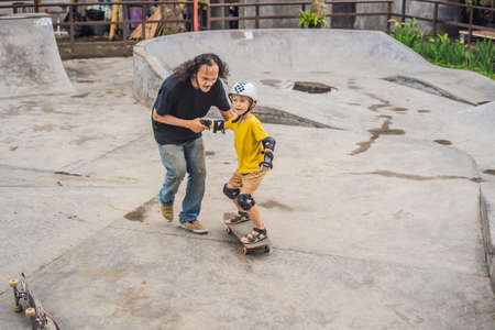 Athletic boy learns to skateboard with a trainer in a skate park. Children education, sportsの写真素材