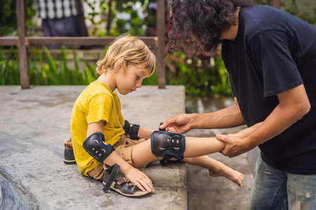 Trainer helps the boy to wear knee pads and armbands before training skate boardの写真素材