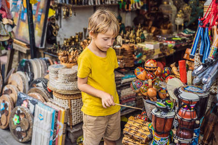 Boy at a market in Ubud, Bali. Typical souvenir shop selling souvenirs and handicrafts of Bali at the famous Ubud Market, Indonesia. Balinese market. Souvenirs of wood and crafts of local residents. Traveling with children concept. Kids friendly placeの写真素材