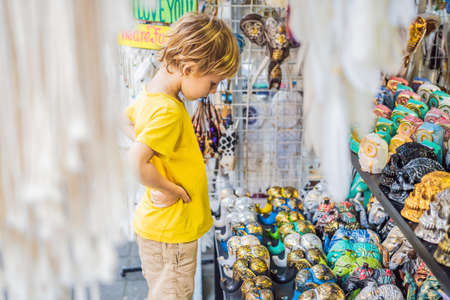 Boy at a market in Ubud, Bali. Typical souvenir shop selling souvenirs and handicrafts of Bali at the famous Ubud Market, Indonesia. Balinese market. Souvenirs of wood and crafts of local residents. Traveling with children concept. Kids friendly placeの写真素材