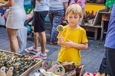 Boy at a market in Ubud, Bali. Typical souvenir shop selling souvenirs and handicrafts of Bali at the famous Ubud Market, Indonesia. Balinese market. Souvenirs of wood and crafts of local residents. Traveling with children concept. Kids friendly placeの写真素材