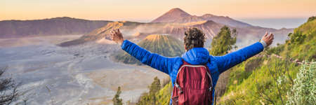 BANNER, LONG FORMAT Young man meets the sunrise at the Bromo Tengger Semeru National Park on the Java Island, Indonesia. He enjoys magnificent view on the Bromo or Gunung Bromo on Indonesian, Semeru and other volcanoes located inside of the Sea of Sand within the Tengger Caldera. One of the most famous volcanic objects in the world. Travel to Indonesia conceptの写真素材