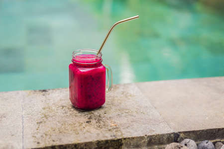 Dragon fruit smoothie with steel drinking straw on pool background.の写真素材