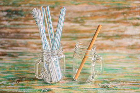 Bamboo drinking straw vs disposable straws on wooden painted background. Zero waste concept.