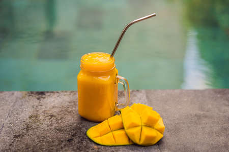 Mango smoothie and steel drinking straw on pool background.