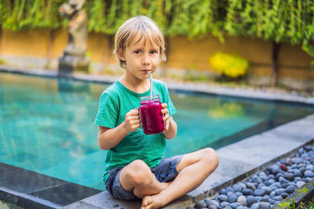 Boy drinks dragon fruit smoothie with steel drinking straw by the poolの写真素材