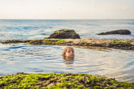 Boy tourist on Pantai Tegal Wangi Beach sitting in a bath of sea water, Bali Island, Indonesia. Bali...