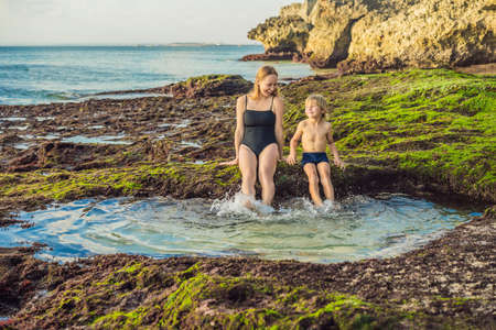 Mother and son tourists on Pantai Tegal Wangi Beach sitting in a bath of sea water, Bali Island, Indonesia. Bali Travel Concept. Traveling with children concept. Kids friendly placesの写真素材