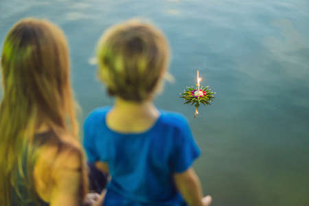 Mom and son tourists holds the Loy Krathong in her hands and is about to launch it into the water. Loy Krathong festival, People buy flowers and candle to light and float on water to celebrate the Loy Krathong festival in Thailandの写真素材