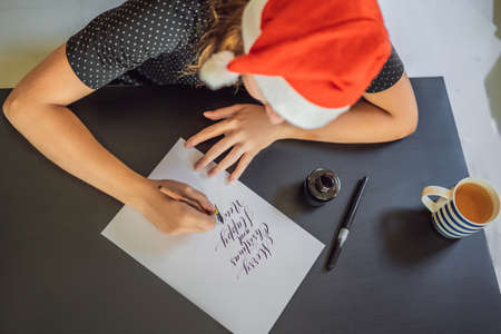 Merry christmas and a happy new year. Calligrapher Young Woman writes phrase on white paper....
