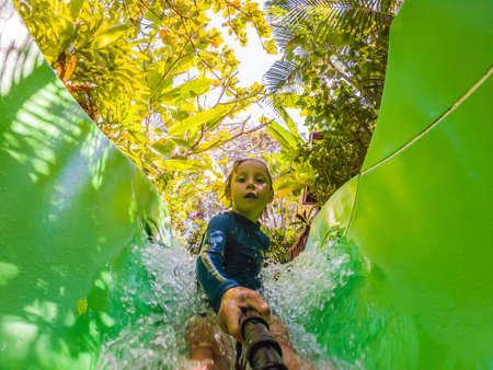 Happy boy on water slide in a swimming pool having fun during summer vacation in a beautiful...
