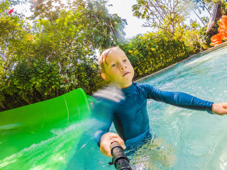 Happy boy on water slide in a swimming pool having fun during summer vacation in a beautiful tropical resortの写真素材