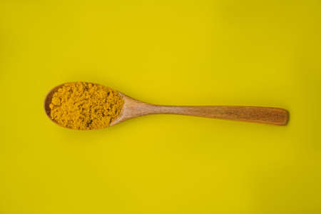 Turmeric powder in a wooden spoon on a yellow backgroundの写真素材