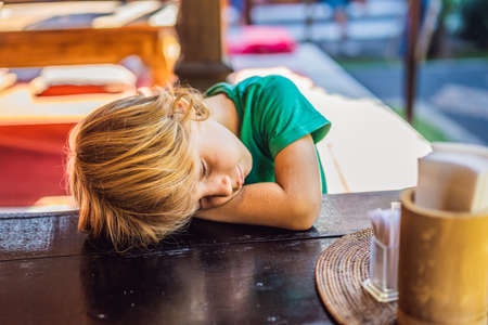 Emotional boy at a table in a cafe. Cute little boy sitting in outdoor restaurant on summer day. child in a cafe waiting for his orderの写真素材