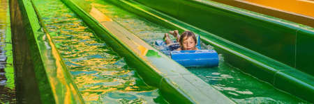 Happy boy on water slide in a swimming pool having fun during summer vacation in a beautiful...