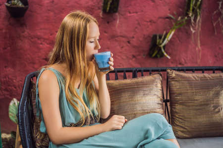 Young woman having a mediterranean breakfast seated at sofa and drinks Trendy drink: Blue latte. Hot butterfly pea latte or blue spirulina latteの写真素材