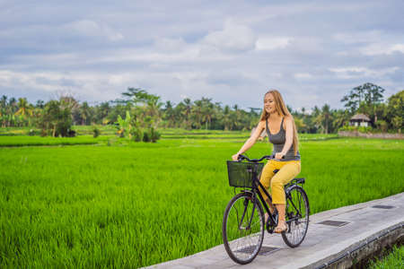 A young woman rides a bicycle on a rice field in Ubud, Bali. Bali Travel Conceptの写真素材