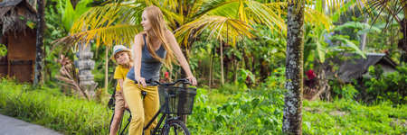 Mother and son ride a bicycle on a rice field in Ubud, Bali. Travel to Bali with kids concept BANNER, LONG FORMATの写真素材