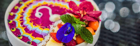 Smoothie bowl with tropical fruits, decorated with a pattern of colorful yogurt with turmeric and...