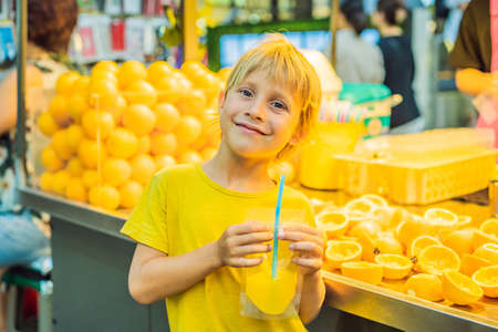Little boy tourist drinks freshly squeezed orange juice on a walking street of Seoul. Fresh juice is a popular tourist attraction in Korea. Travel to Korea concept. Traveling with children conceptの写真素材