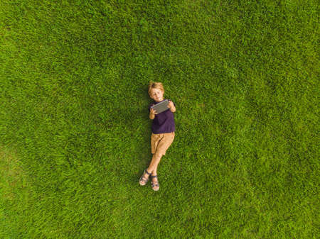 Boy lying on the grass in the park and looks at the tablet.の写真素材