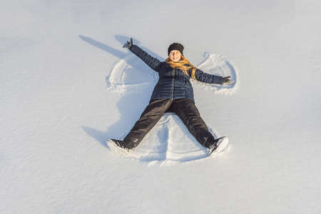 Woman warmly clothed in a cold winter forest makes snow angel figure at park.の写真素材