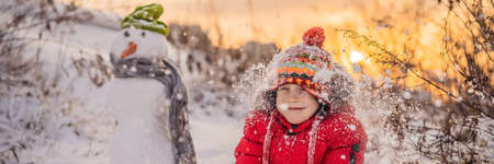 Cute boy in red winter clothes builds a snowman.の写真素材