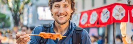 Young man tourist eating Typical Korean street food on a walking street of Seoul.の写真素材