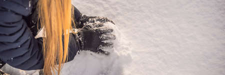 Young woman rolling giant snowball to make snowman