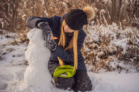Young woman rolling giant snowball to make snowmanの写真素材