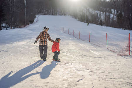 Mother teaches son snowboarding. Activities for children in winter. Childrens winter sport. Lifestyleの写真素材