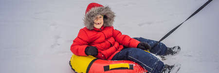 Child having fun on snow tube. Boy is riding a tubing. Winter fun for children BANNER, LONG FORMATの写真素材