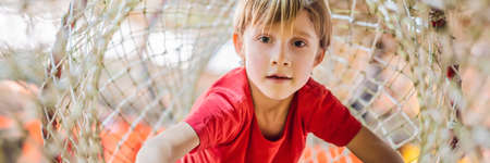 Boy crawls on a net in an obstacle course BANNER, LONG FORMATの写真素材
