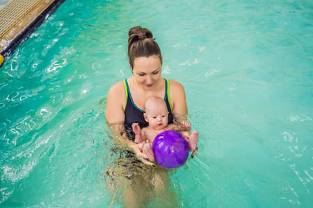 Beautiful mother teaching cute baby girl how to swim in a swimming pool. Child having fun in water with momの写真素材