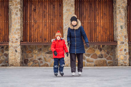 young mother teaching her little son ice skating at outdoor skating rink. Family enjoy winter on ice-rink outdoorsの写真素材