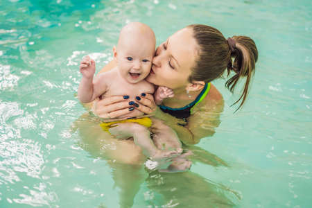 Beautiful mother teaching cute baby girl how to swim in a swimming pool. Child having fun in water with momの写真素材