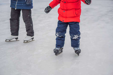 young mother teaching her little son ice skating at outdoor skating rink. Family enjoy winter on ice-rink outdoors.の写真素材