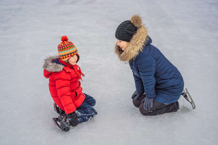 young mother teaching her little son ice skating at outdoor skating rink. Family enjoy winter on...