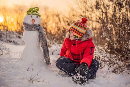 Cute boy in red winter clothes builds a snowman. Winter Fun Outdoor Concept.の写真素材