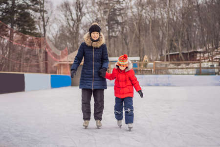 young mother teaching her little son ice skating at outdoor skating rink. Family enjoy winter on ice-rink outdoorsの写真素材
