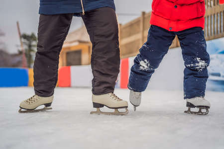 young mother teaching her little son ice skating at outdoor skating rink. Family enjoy winter on ice-rink outdoors.の写真素材
