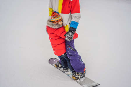 Dad and son ride the same snowboard, breaking safety precautions.の写真素材