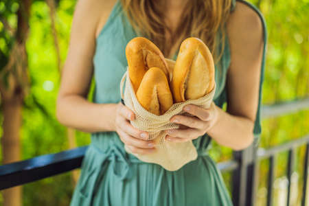 Reusable grocery bags with bread in the hands of a young woman. Zero waste shopping. Zero waste...