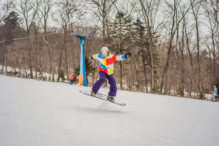 Young man jumping with a snowboard in the mountains